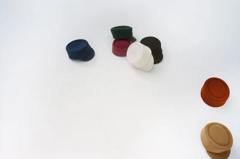 Collection of colorful pillbox hats arranged on a white surface, showcasing different shades including blue, green, red, white, and brown.