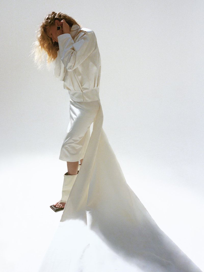 Model in white structured jacket and matching skirt with long train against white background
