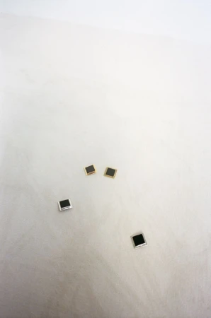 Four square stud earrings, two with silver trim and two with gold trim, arranged on a white surface with subtle textural details.