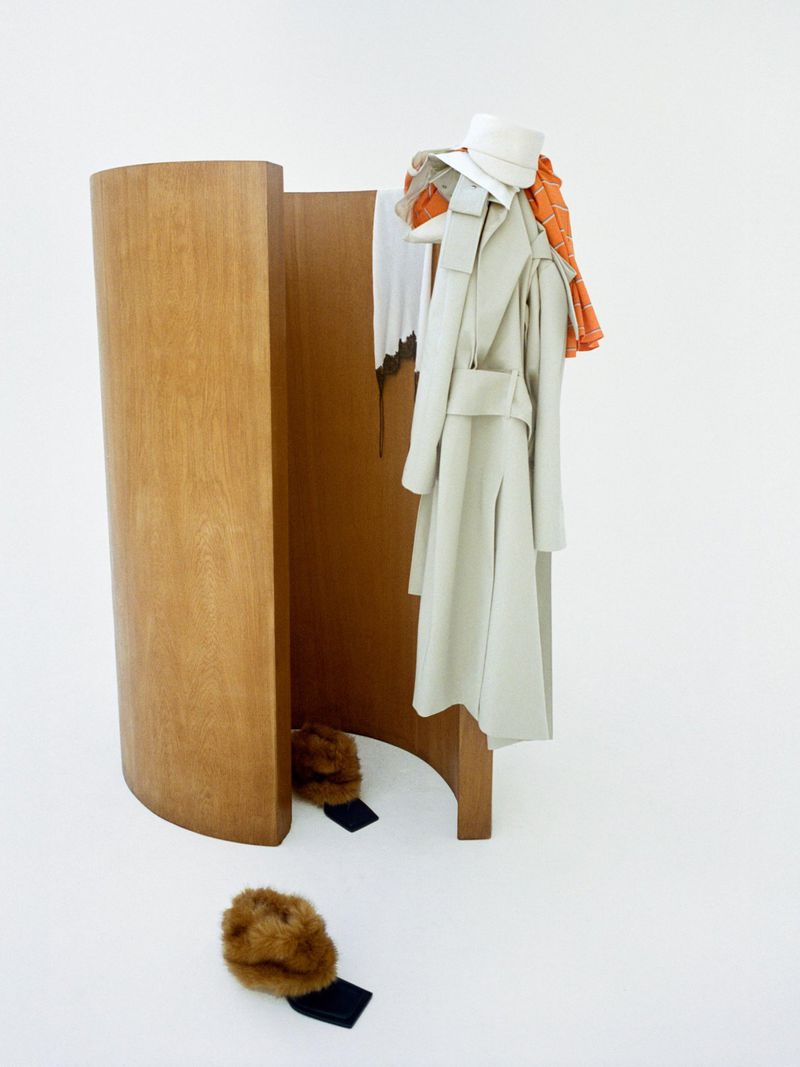 Still-life shot in a white studio featuring a wooden room divider with a neutral-colored coat, a white hat, and fur hats.