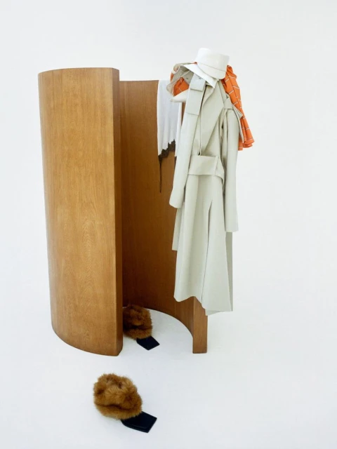 Still-life shot in a white studio featuring a wooden room divider with a neutral-colored coat, a white hat, and fur hats.