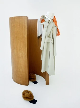 Still-life shot in a white studio featuring a wooden room divider with a neutral-colored coat, a white hat, and fur hats.