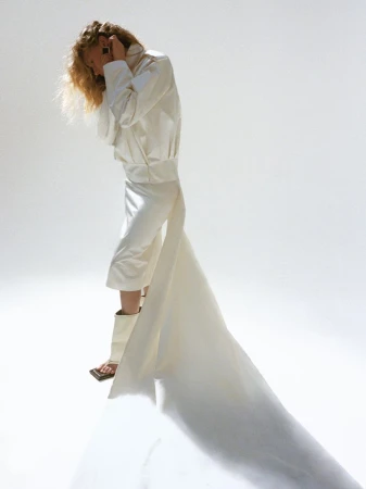 Model in white structured jacket and matching skirt with long train against white background