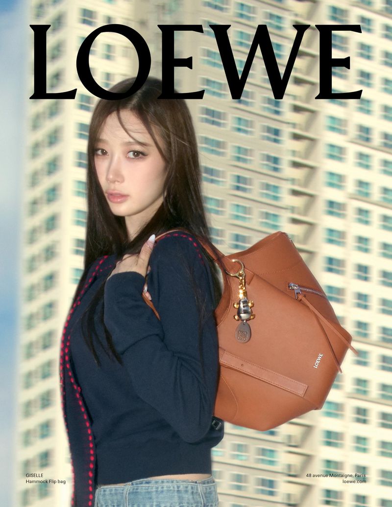 Asian woman models Loewe handbag outdoors with city building in the background. Fashion editorial shot. Loewe logo visible.