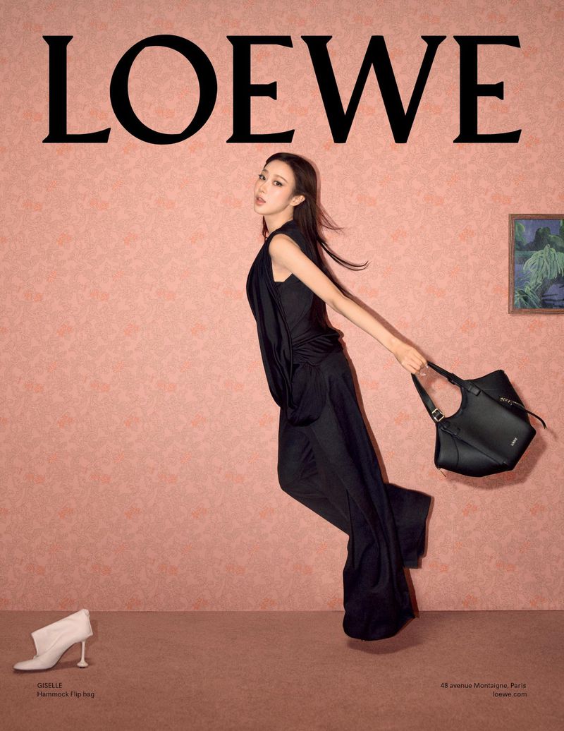 Fashion editorial shot featuring a stylish woman in black attire, holding a black handbag, posing against a peach-colored patterned background.