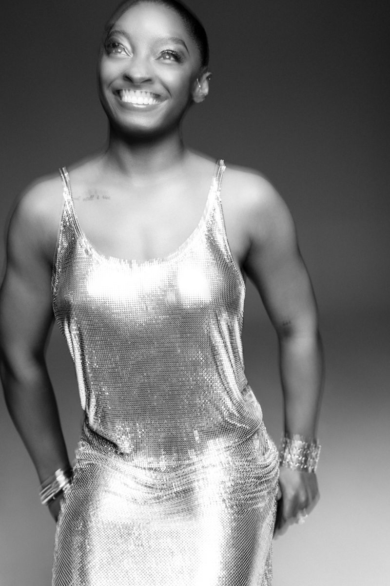 Black and white portrait of a smiling African-American woman in a metallic dress with silver bracelets, looking up in soft light.