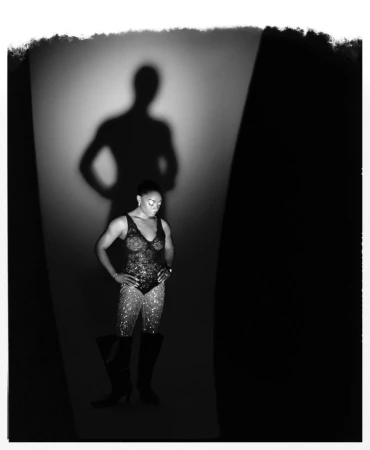 Artistic black and white studio portrait of an athletic African American woman in a lace bodysuit posing in front of her shadow.