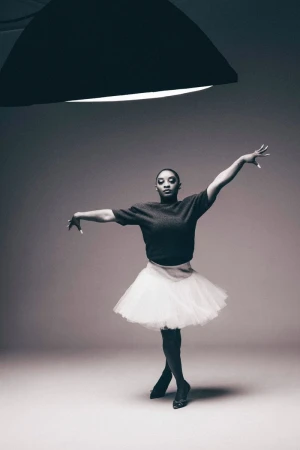 Young woman in ballet pose wearing tutu in studio under lighting equipment. Dance or fashion photography with ballerina in studio.