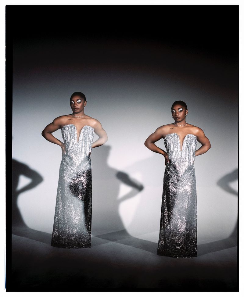 Woman in shimmering silver gown poses, hands on hips, shadow detail, studio shot, bright lighting, elegant formal wear, dark hair, light skin.