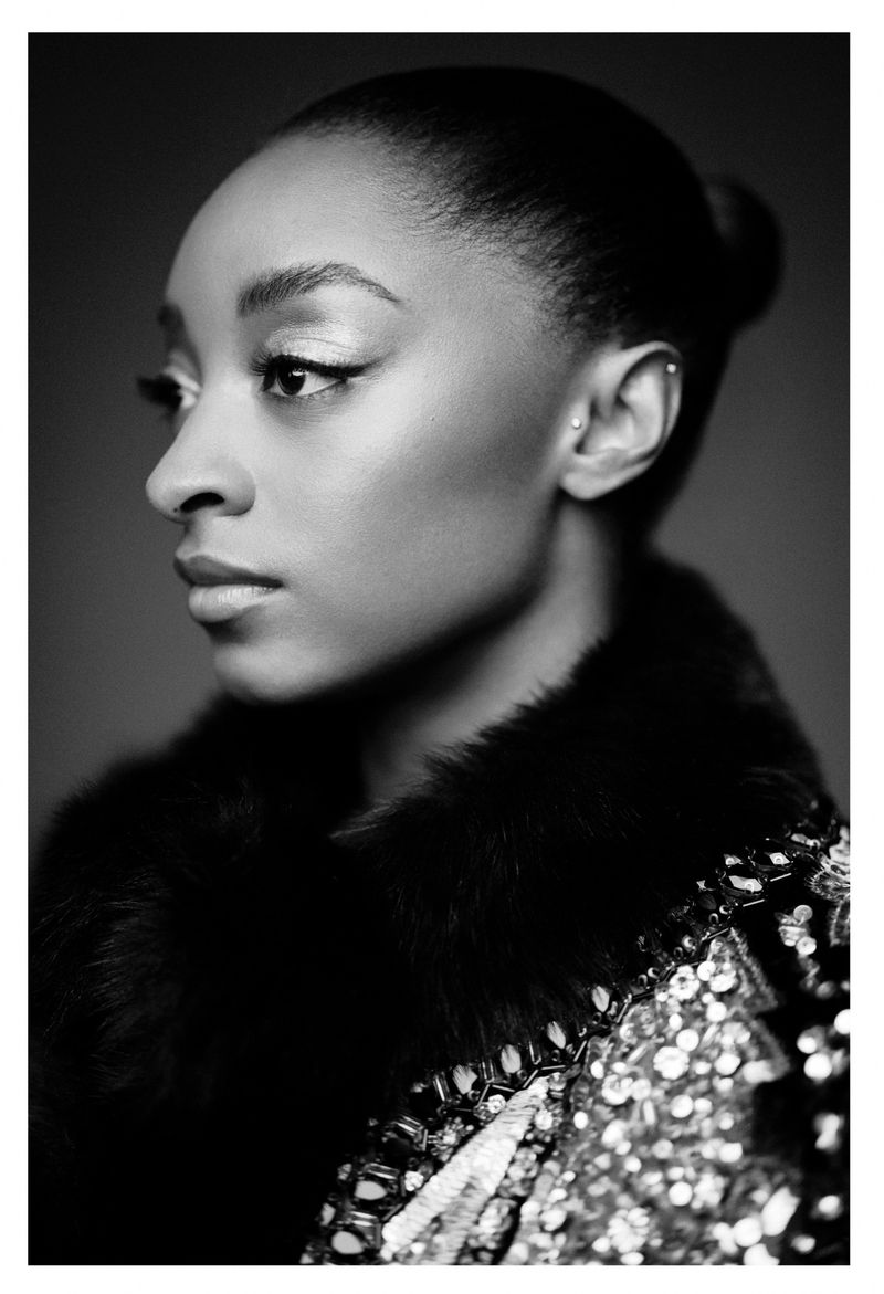 Black and white portrait of an adult woman looking off to the side, wearing a sequined garment with fur trim, in a studio setting.