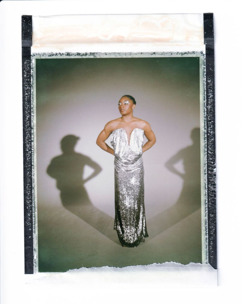Elegant woman with short hair poses in a silver gown with shadows behind her. Studio shot with a blank background.