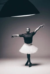 Simone Biles in a dark short-sleeve top and white tulle tutu skirt posing in a ballet stance under a studio softbox light.