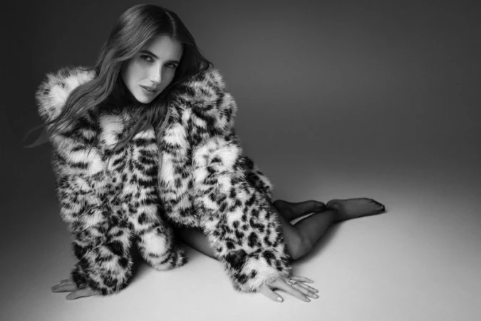 Black and white editorial portrait of actress Emma Roberts wearing a patterned faux fur coat on a seamless studio backdrop.