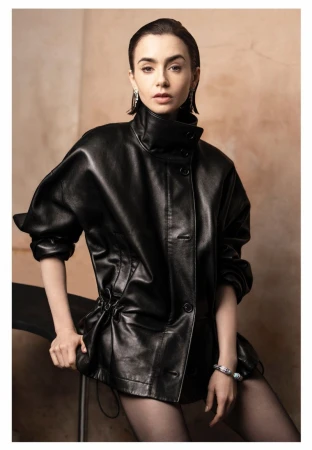 Lily Collins seated in an oversized black leather jacket with slicked-back hair against a warm textured backdrop.