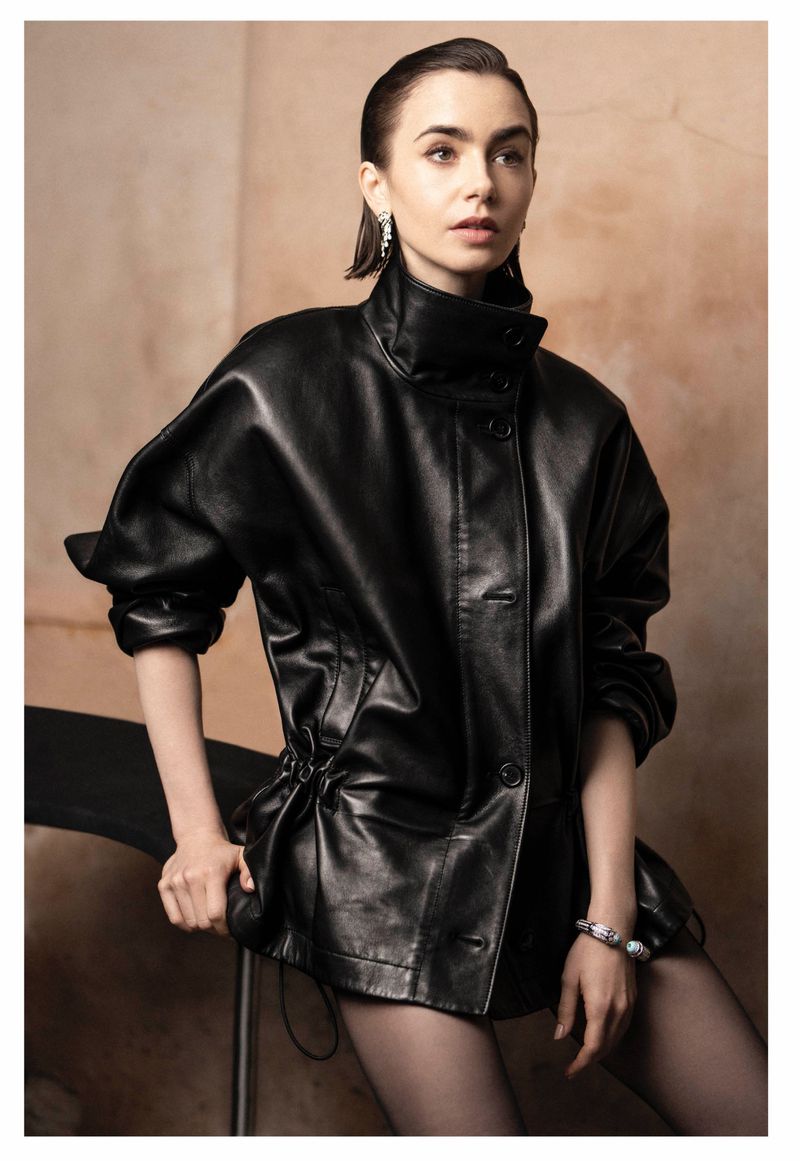 Portrait of a woman with sleek dark hair wearing a black leather jacket with a high collar and accessorized with jewelry.