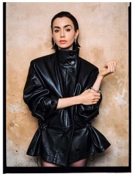 Lily Collins wearing an oversized black leather jacket with a high collar against a textured beige wall.