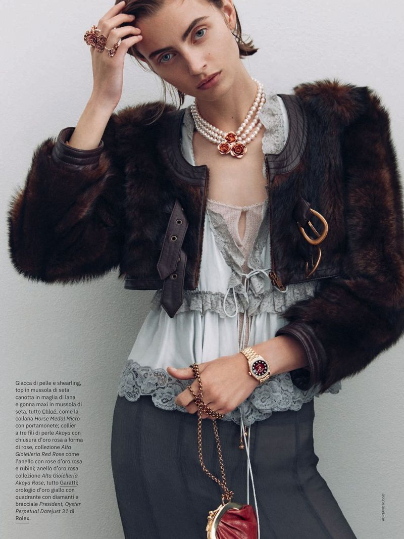 Fashion editorial shot: woman in a fur jacket, tiered pearl necklace with floral accents, wristwatch, skirt, holding a red handbag.