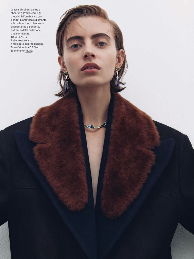Woman in dark coat with fur collar, wearing statement earrings and necklace in a studio setting, professional shot. Beauty and fashion editorial.