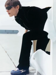 Model wearing dark sunglasses and black apparel posing dynamically through a white paper cutout structure