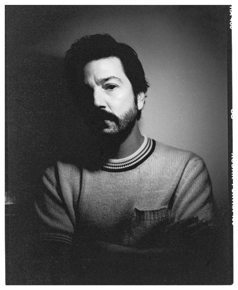 Black and white portrait of an adult male with a beard, wearing a striped-collar sweater. The man is illuminated by side lighting.