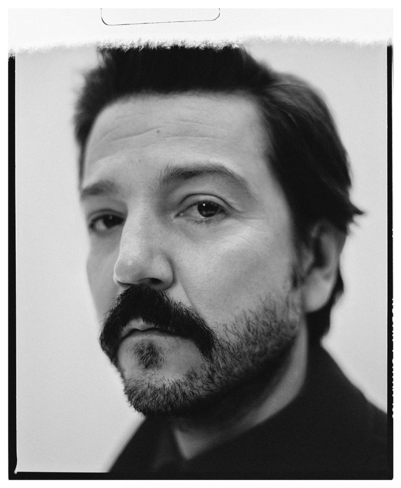 Striking black-and-white portrait of a man with a mustache and beard, captured in a close-up shot against a plain background.