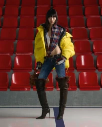 Model Chun Jin wearing a yellow puffer jacket and over-the-knee boots standing in front of red stadium seats for Dsquared2 Pre-Fall 2026.