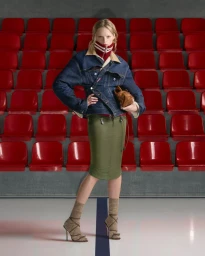 Hanne Gaby Odiele wearing a denim jacket and olive green midi skirt posing in front of red stadium seats.