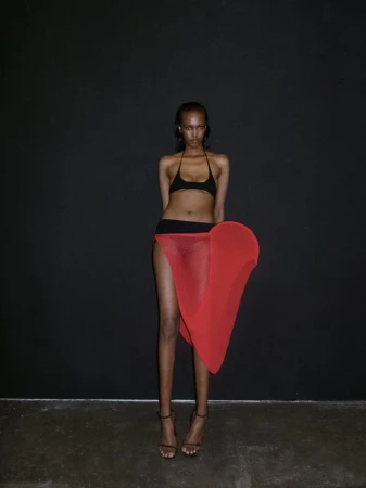 Woman in bikini and red skirt poses against black backdrop, showcasing fashion and style with studio lighting and a confident expression.