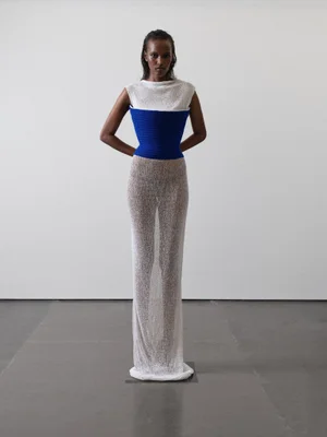 Model Maryamo Musse wearing a structured white and blue dress against a plain white studio backdrop.