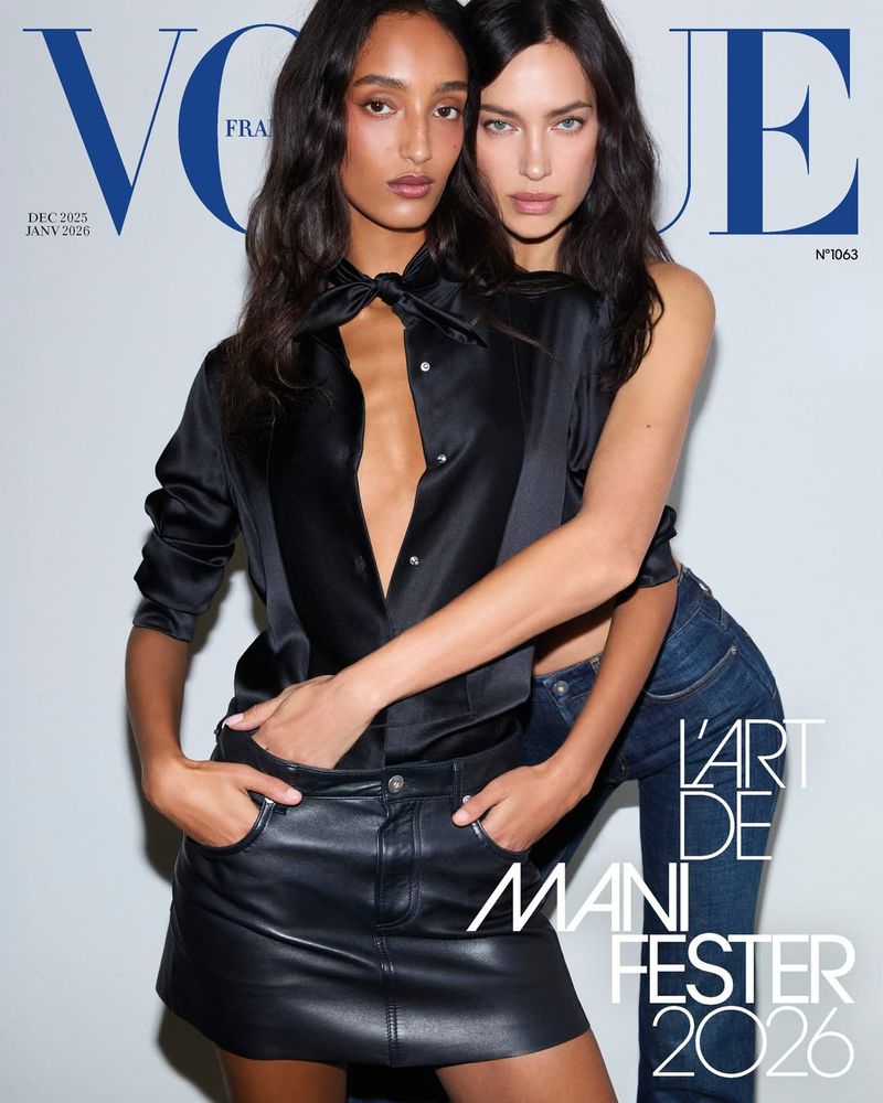 Two women pose on the cover of Vogue magazine. One wears a black satin blouse and leather skirt; the other wears jeans and a top.