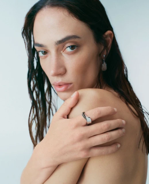 Close-up studio shot of an adult female with dark hair, fair skin, nude shoulders, wearing a silver ring, looking at the camera.