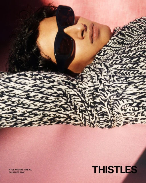 Portrait of a person in sunglasses and a knit sweater lying on a pink surface, with the brand name 'THISTLES' visible below.