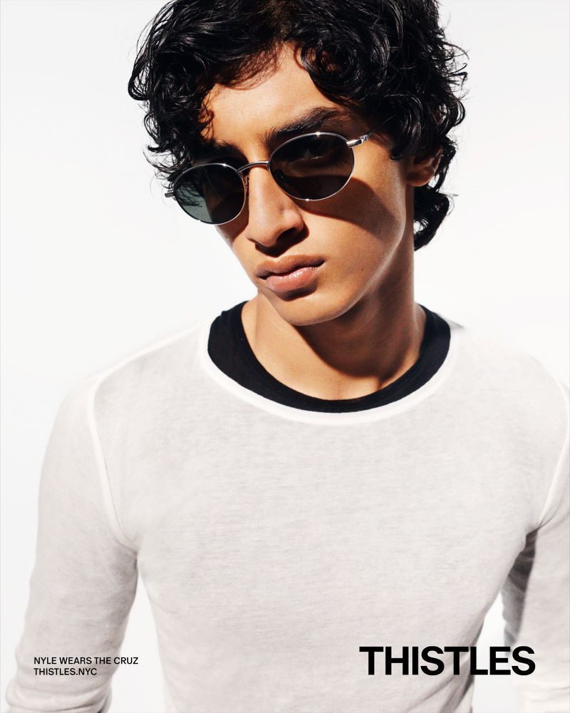 Close-up of a male model wearing a white long sleeve shirt and sunglasses against a white background, showcasing fashion and style.
