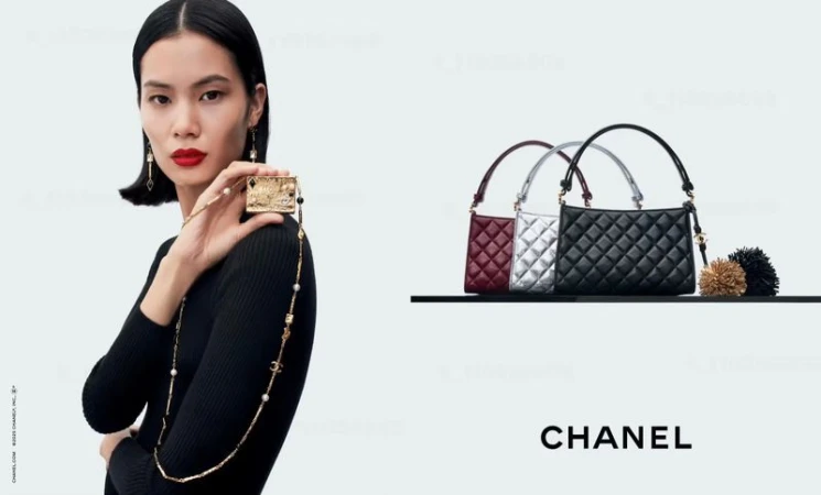 A woman in a black top holds a small embellished object, accessorized with a necklace and earrings, alongside Chanel handbags.