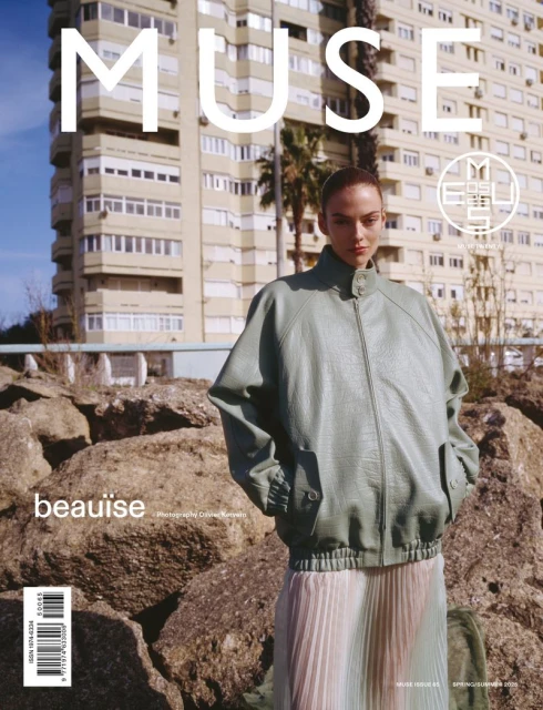 Fashion magazine cover featuring a young adult woman in a jacket and skirt, posed against a building and rock backdrop.