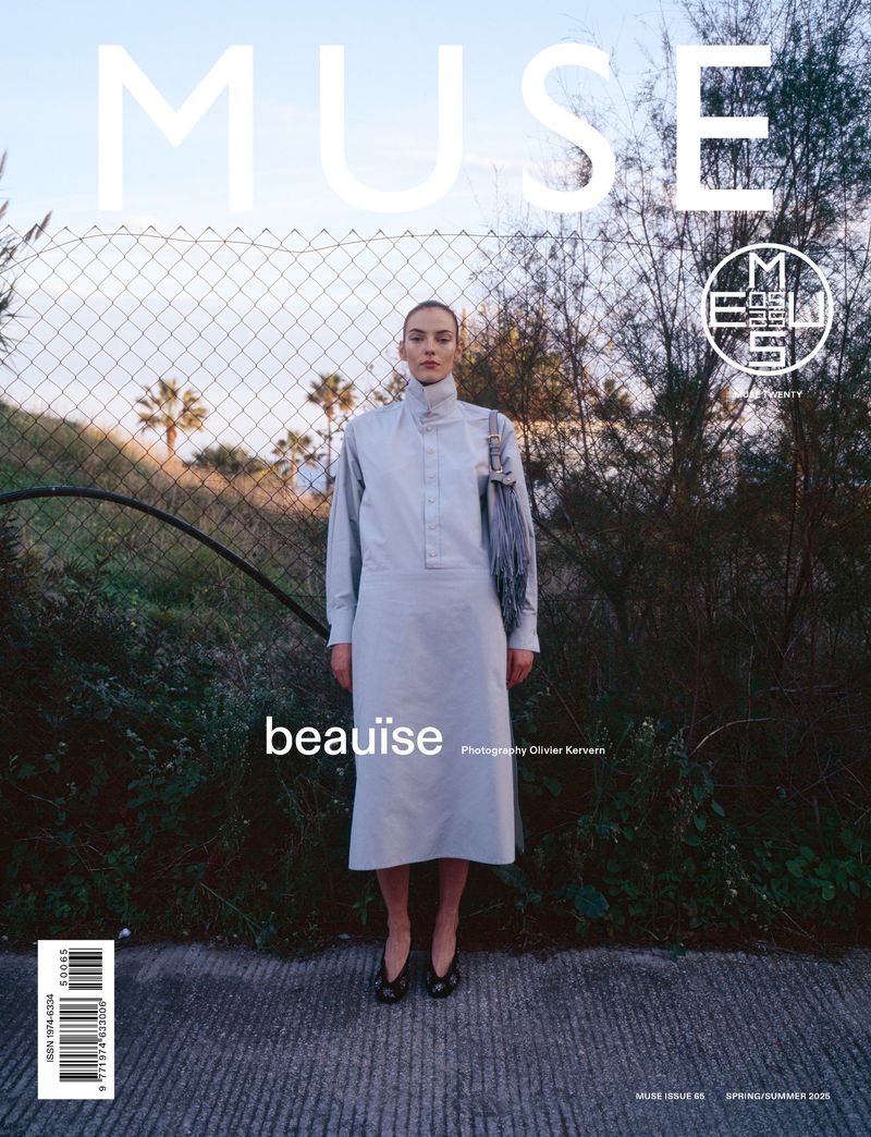 Magazine cover featuring a model in a light blue dress standing in front of a wire fence and greenery, with the title MUSE.