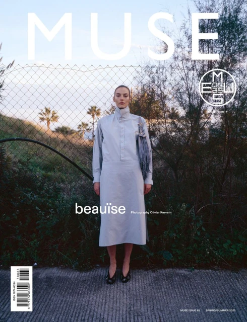 Magazine cover featuring a model in a light blue dress standing in front of a wire fence and greenery, with the title MUSE.