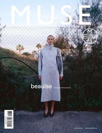 Magazine cover featuring a model in a light blue dress standing in front of a wire fence and greenery, with the title MUSE.