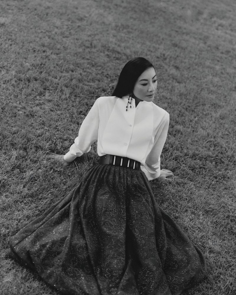 Woman in white shirt and dark flared skirt seated outdoors on grass for Giorgio Armani Crossroads
