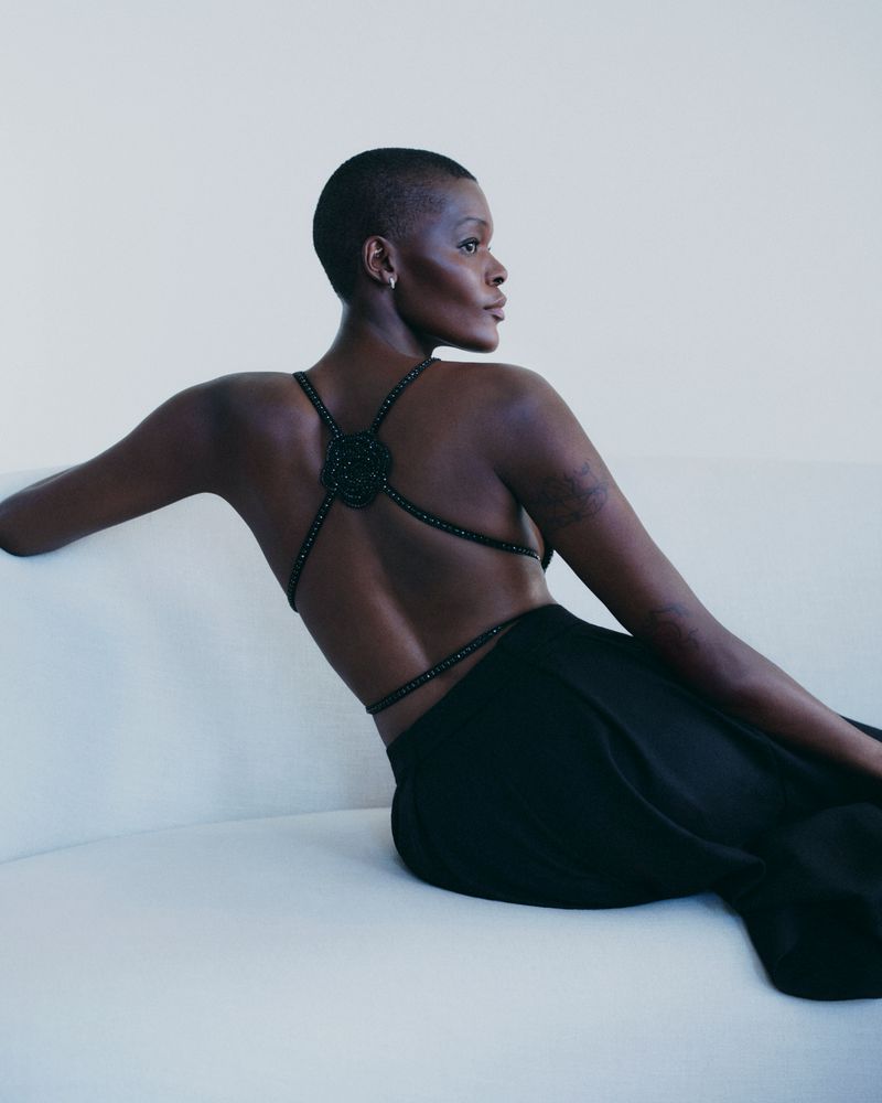 Elegant back view of a short-haired Black female model posing on a white couch in black dress in a minimalist studio setting.