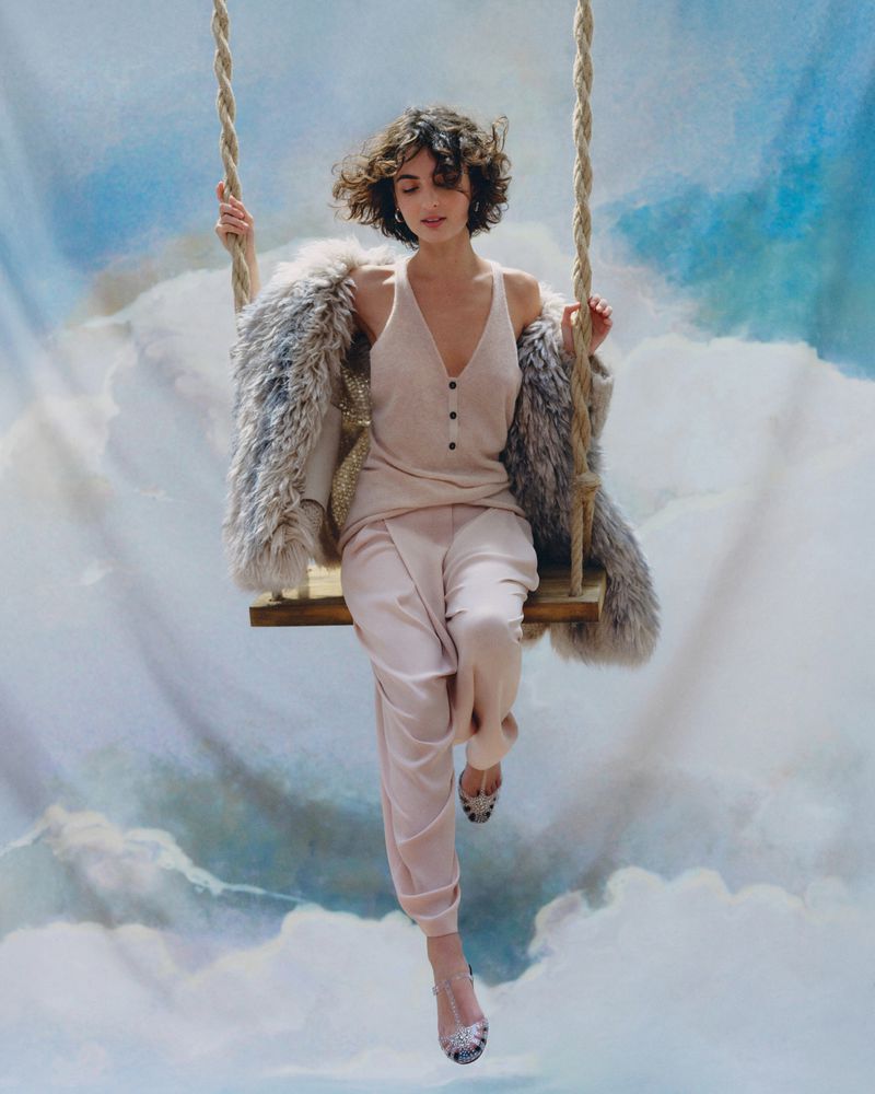 Woman in elegant clothing on a swing, set against a dreamy cloud background, fashion editorial, captured with soft lighting and shallow depth of field.