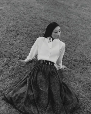 Woman in white shirt and dark flared skirt seated outdoors on grass for Giorgio Armani Crossroads