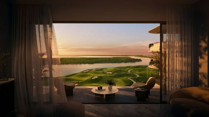 Scenic view from a modern apartment balcony overlooking a lush green golf course and river at sunset with sheer curtains.