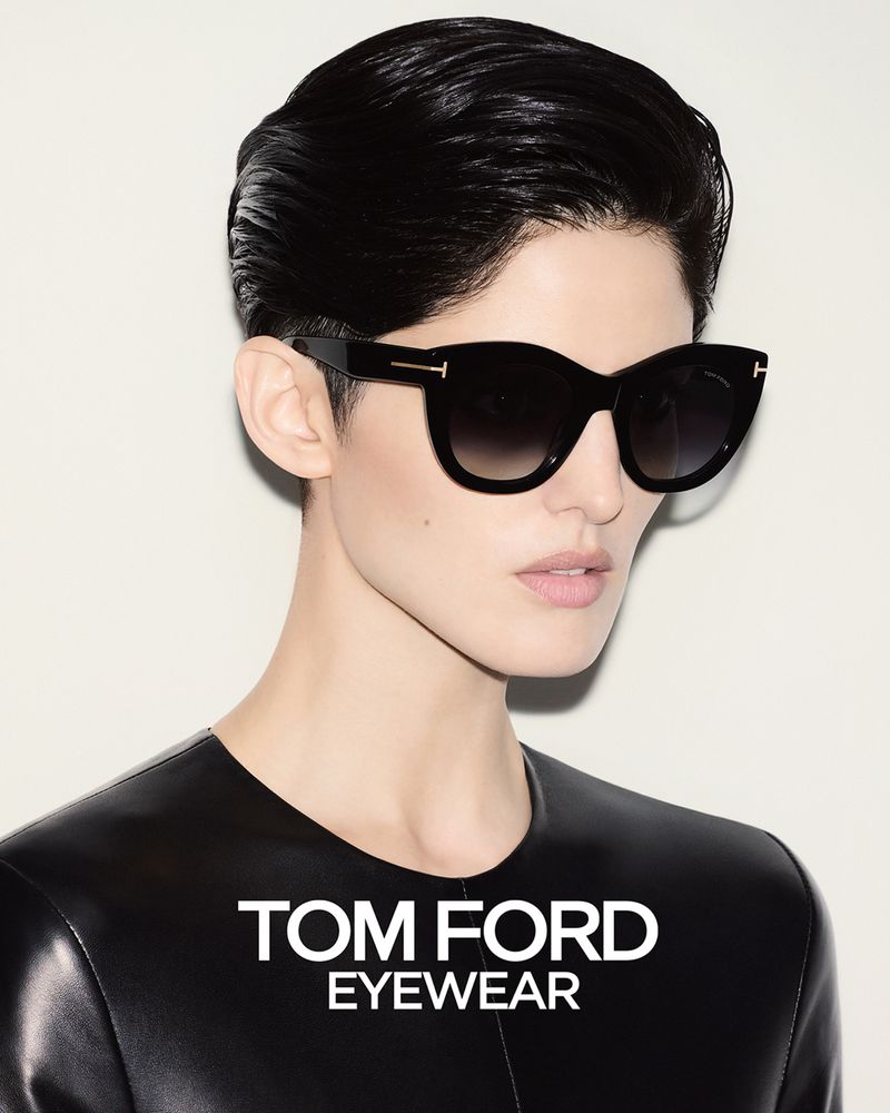 Headshot of a woman with short black hair wearing black sunglasses and a black leather top against a neutral white background.