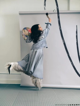 Lucy Liu jumping while painting a black brushstroke on a grey studio backdrop