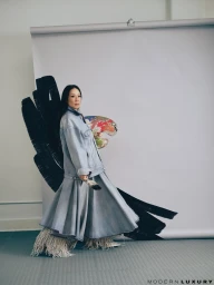 Lucy Liu holding an artist palette and paintbrush wearing a denim jacket and skirt against a grey seamless backdrop