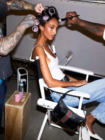 Young woman poses while stylists apply makeup and style her hair with rollers in a studio setting, creating a beauty or fashion shot.