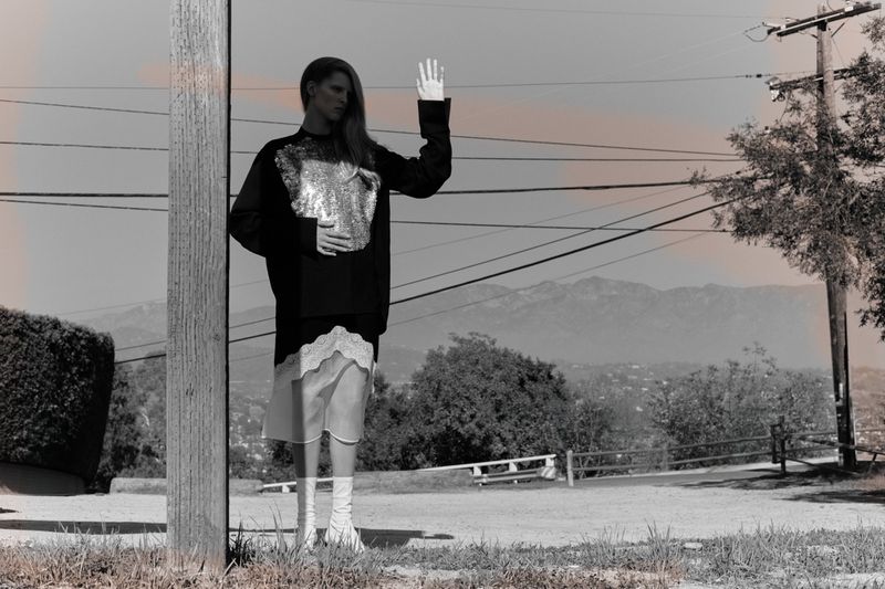 Monochrome outdoor shot of a young adult woman in a sweater and skirt with mountains and utility poles in the background.