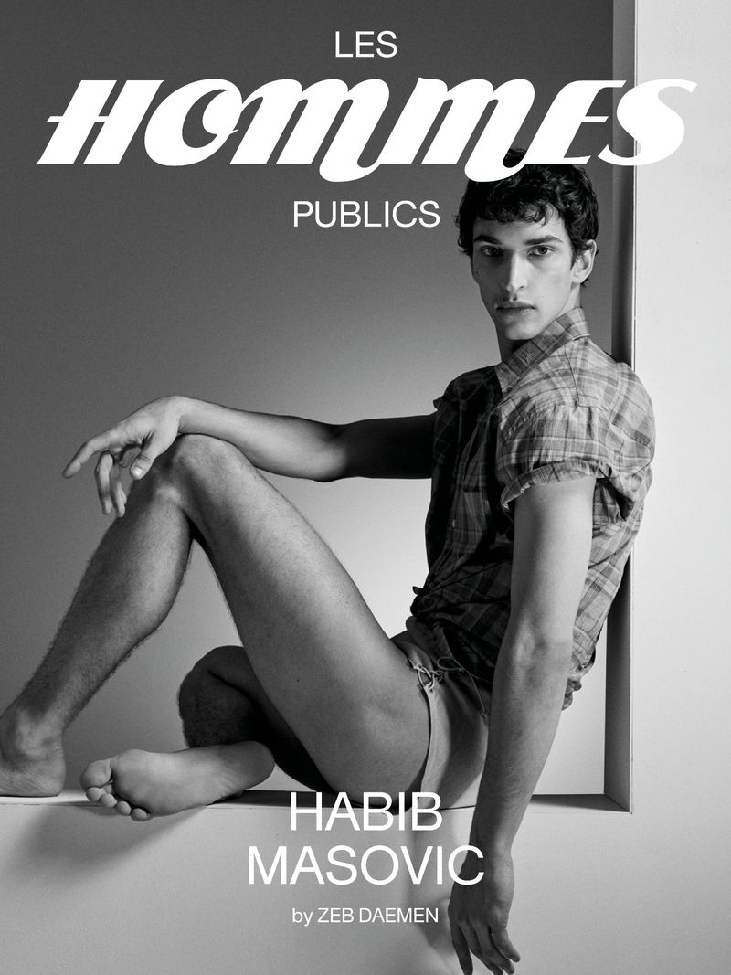 Monochrome portrait of a young adult man in a collared shirt sitting against a wall for a magazine cover photo.