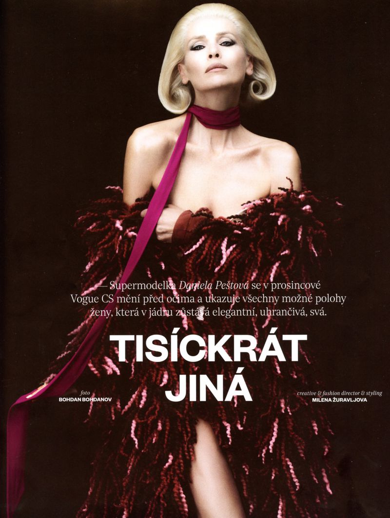 Fashion model in a feathered wrap with magenta ribbon poses indoors against a dark background in a beauty and fashion editorial.